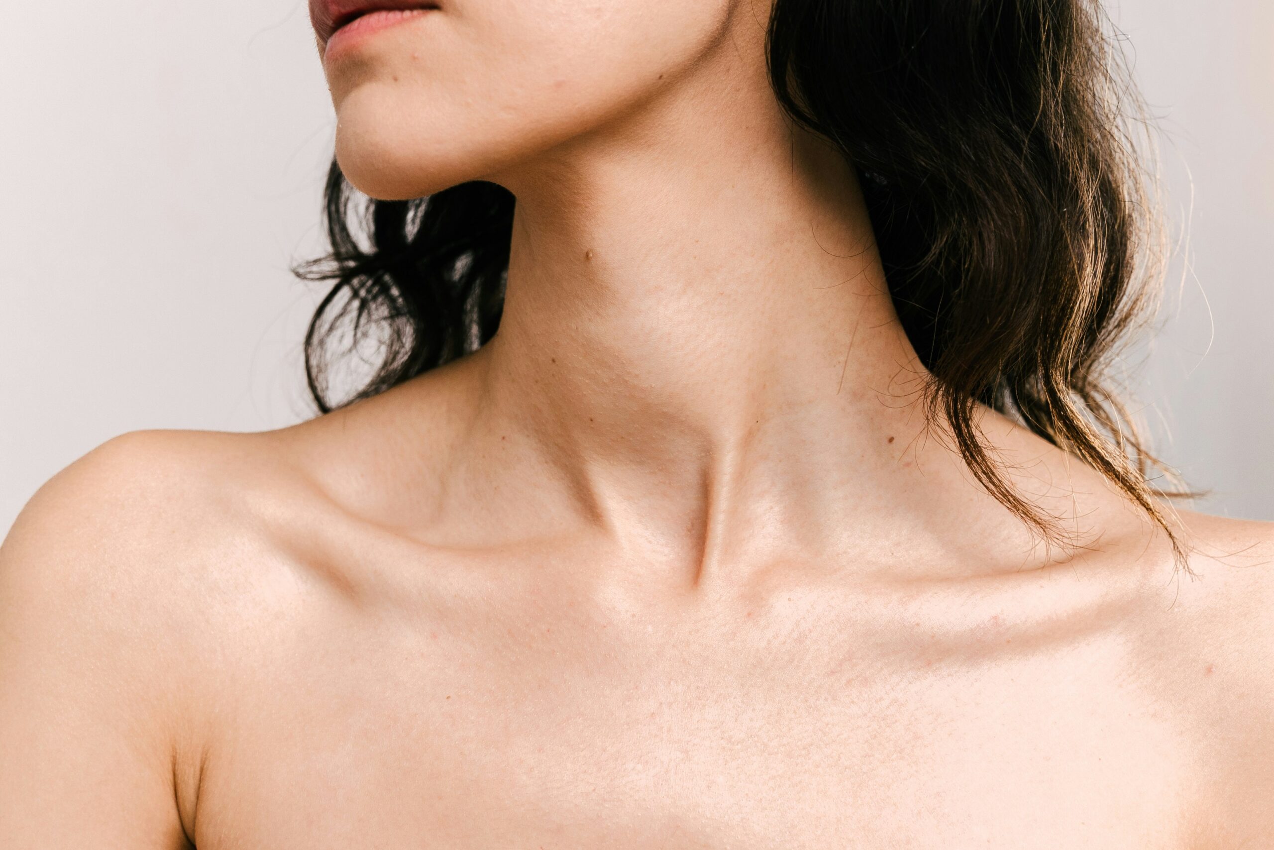 A close-up of a womans bare neck and shoulders, with her head slightly turned to the side, highlighting smooth skin, defined collarbones, and the subtle effects of body contouring.